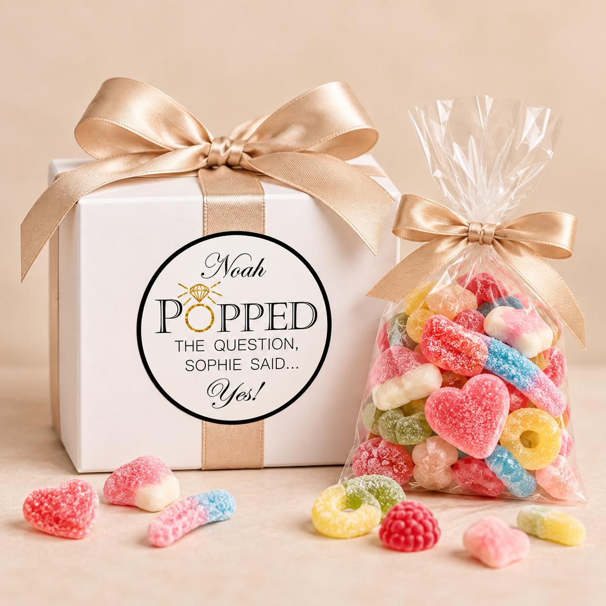 White favor box with gold bow and ‘popped the question’ label beside a bag of gummy candies.