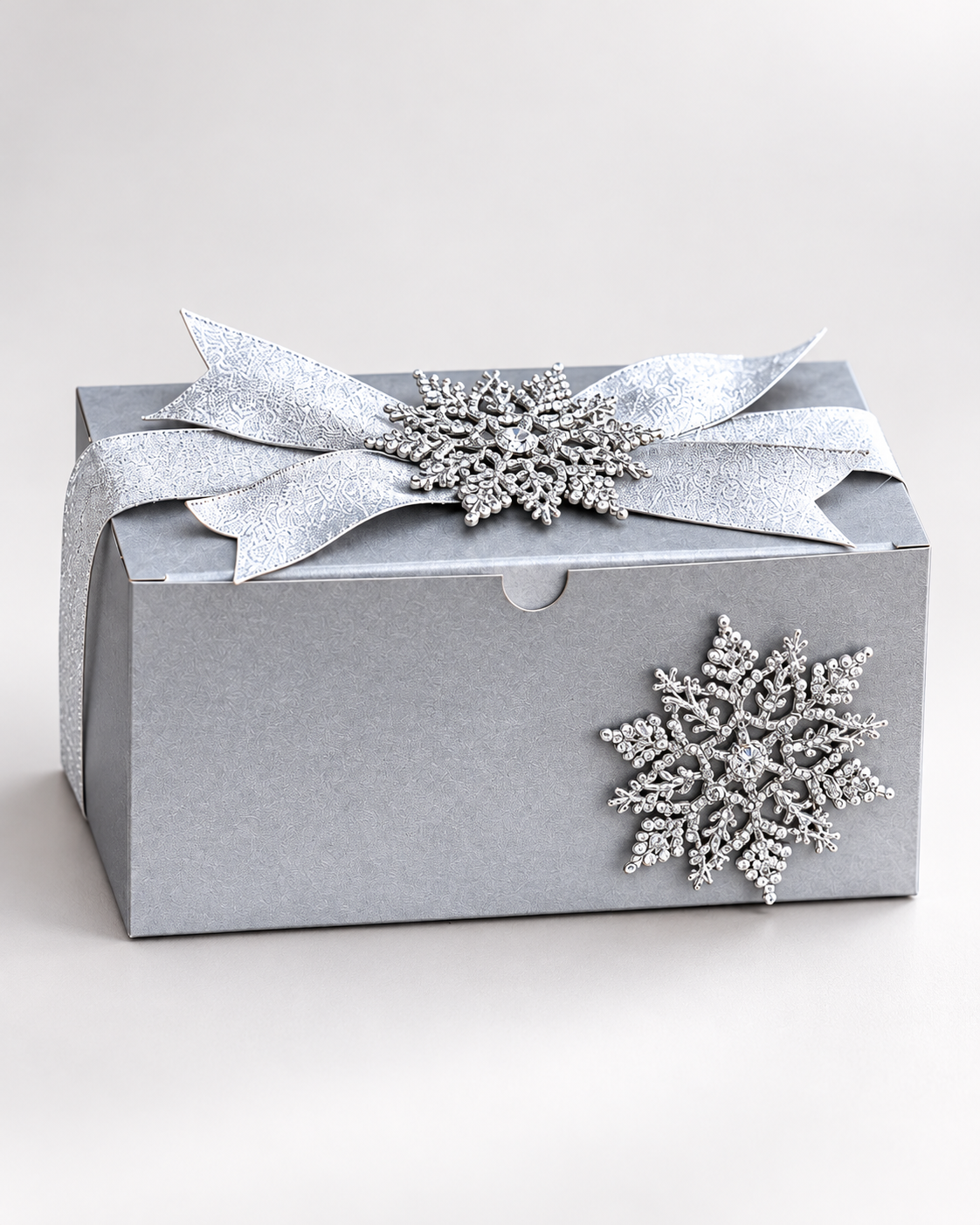 Closed silver gift box tied with patterned ribbon and beaded snowflake ornaments