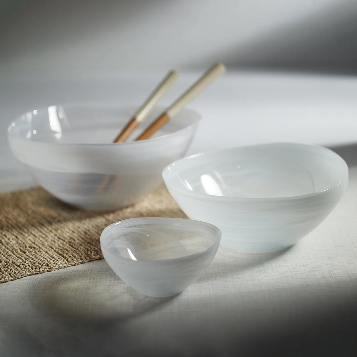 Three white alabaster glass bowls in graduated sizes on woven mat with chopsticks