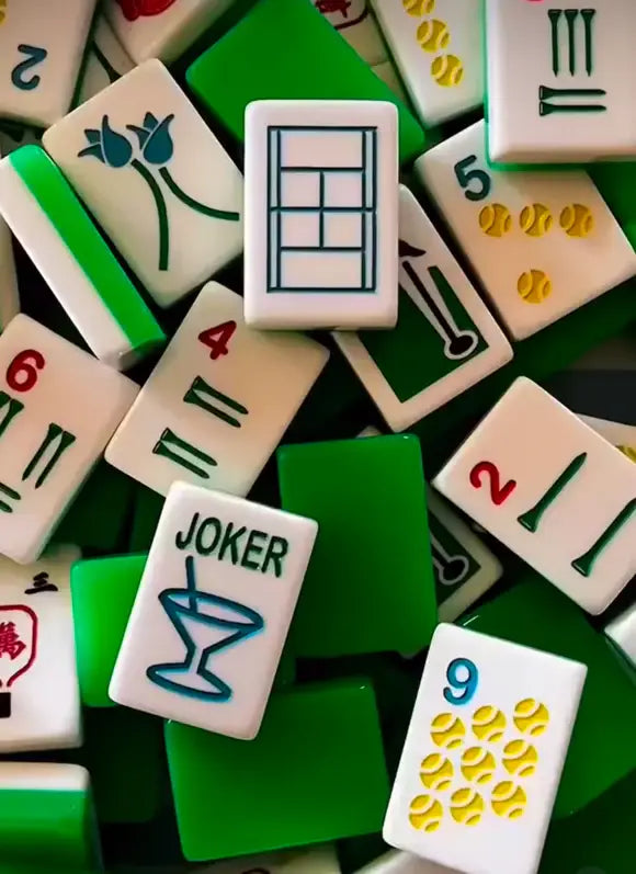 Close-up pile of mahjong tiles showing "JOKER" cocktail-glass tile, tulips, and tennis-ball dots